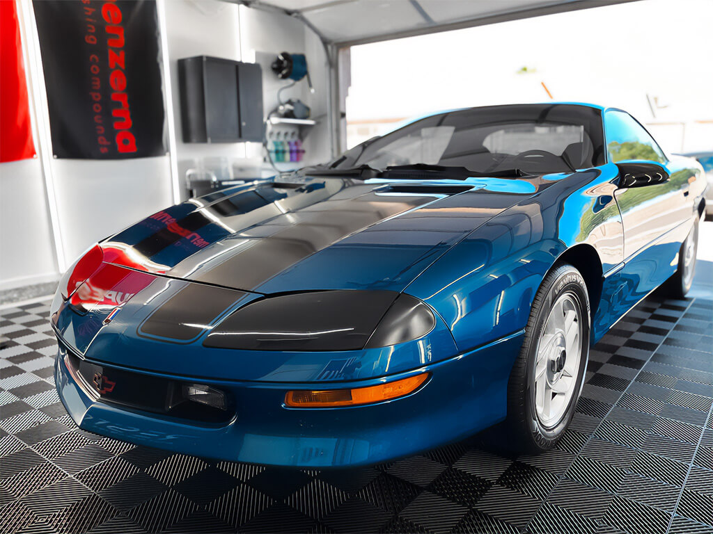 A blue sports car with black stripes and meticulous car detailing inside a detail shop.